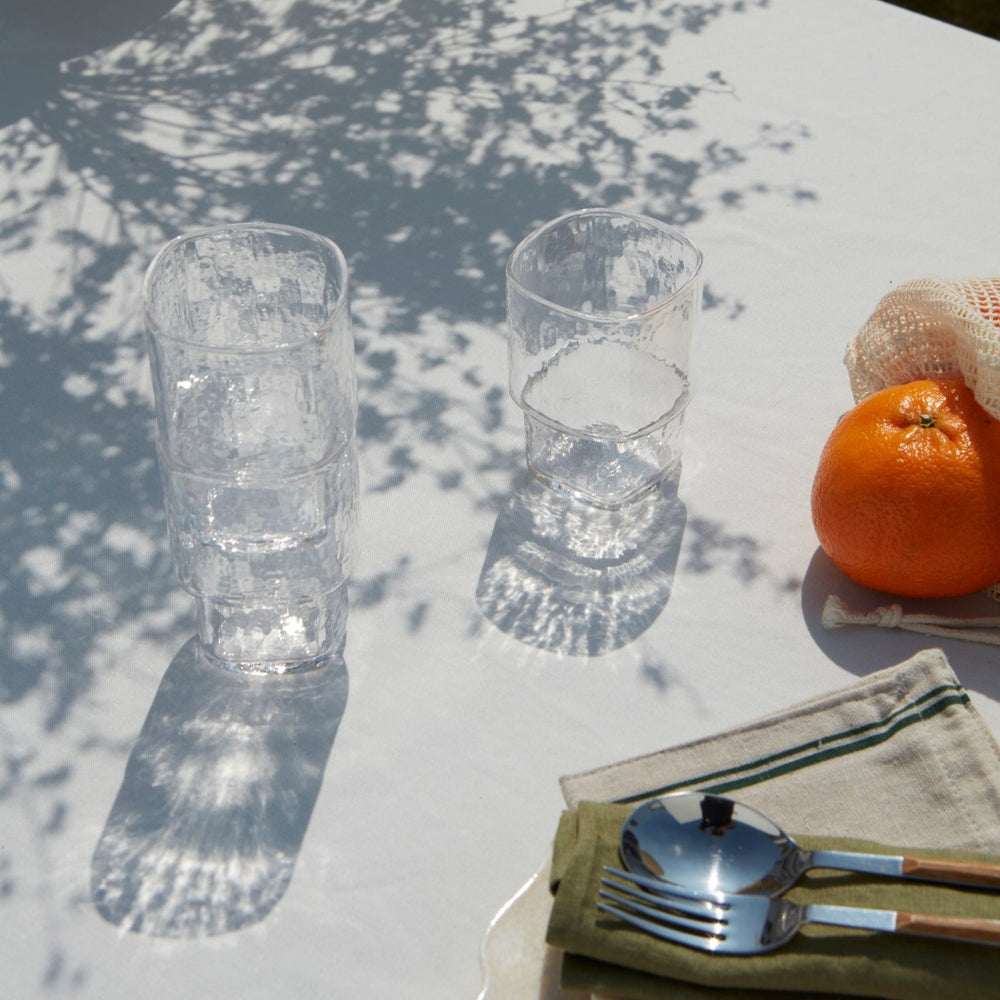 Stackable clear handmade drinking glasses with an angular form and hammered texture on a summer table