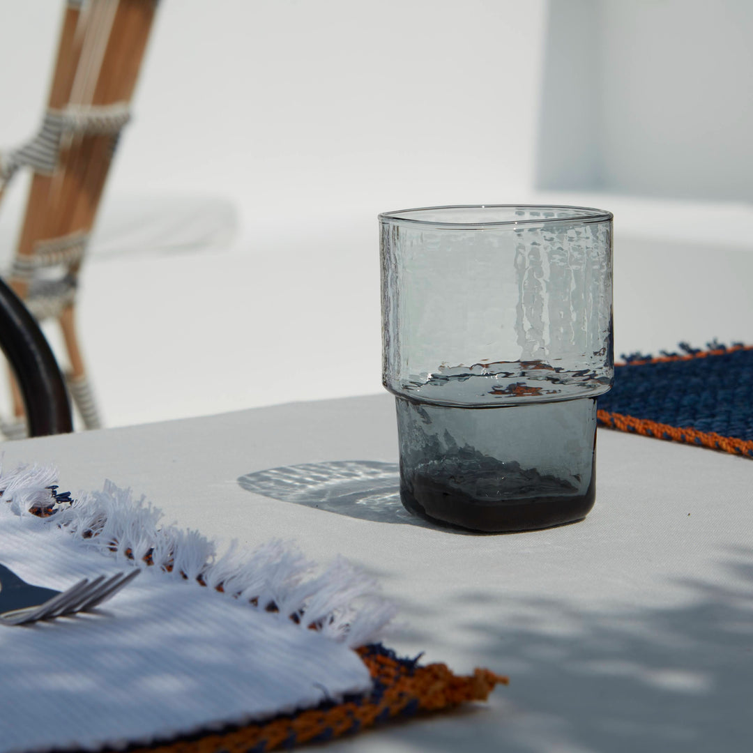 A unique, stackable handmade smoke-grey drinking glasses with an unusual shape and hammered texture on a summer table setting 