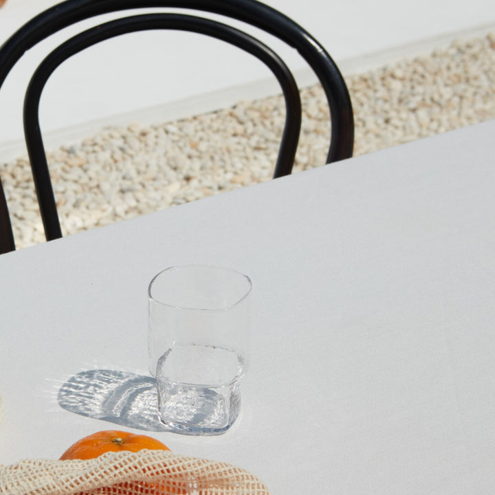 Stackable clear handmade drinking glass with a unique form and hammered texture on a sunny day table setting