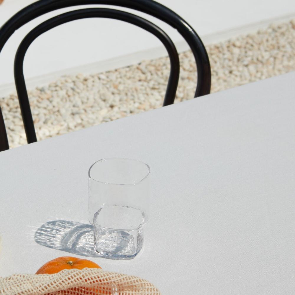 Stackable, angular, slim clear handmade drinking glass with hammered texture on a sunny day table setting
