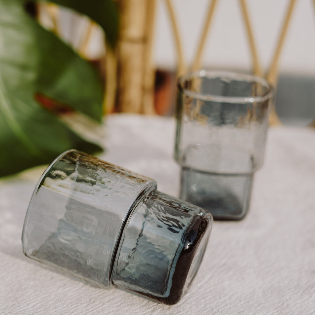 A unique, stackable handmade smoke-grey drinking glasses with an unusual shape and hammered texture 