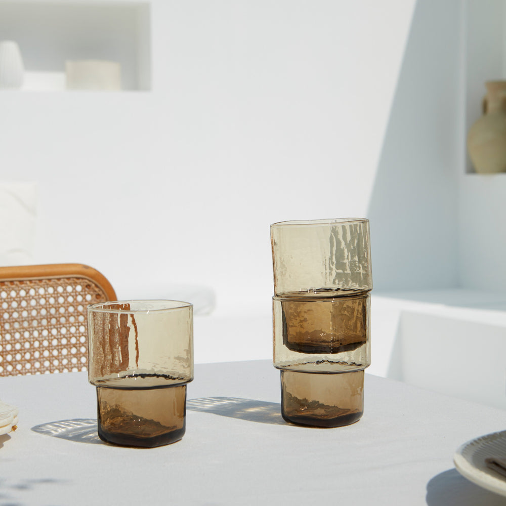 Stackable brown handmade drinking glasses with a unique shape and hammered texture on a sunny summer day