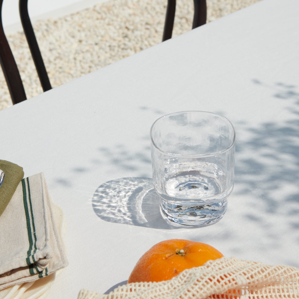 A modern, big, stackable handmade clear drinking glass on a outdoor summer table