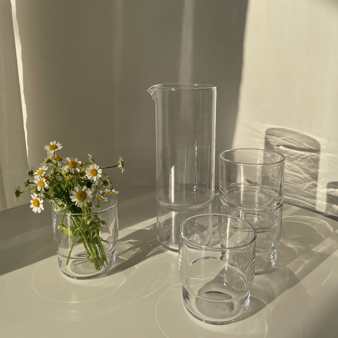A set of 1 litrA set of minimalistic clear handmade glass carafe and matching drinking glasses reflecting sunlight