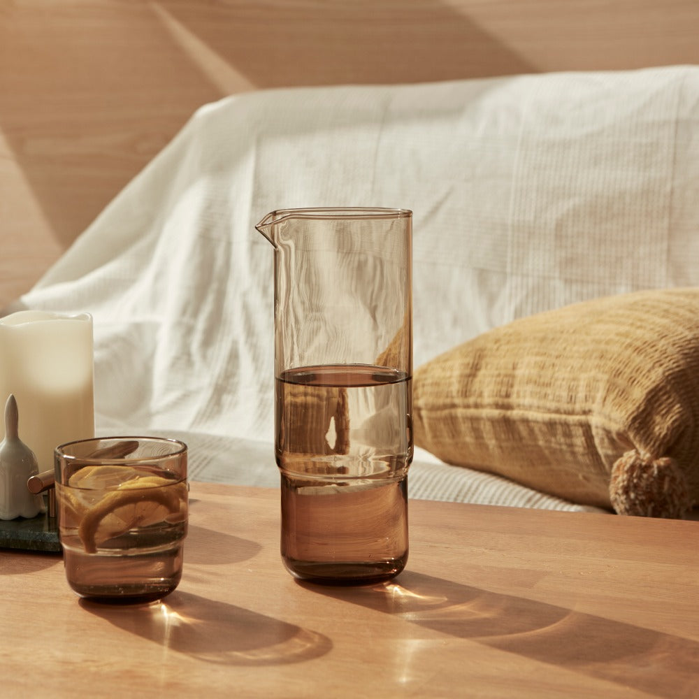 A set of 1 litre cylindrical minimalistic and stylish brown handmade glass carafe and matching drinking glasses on a couch table 