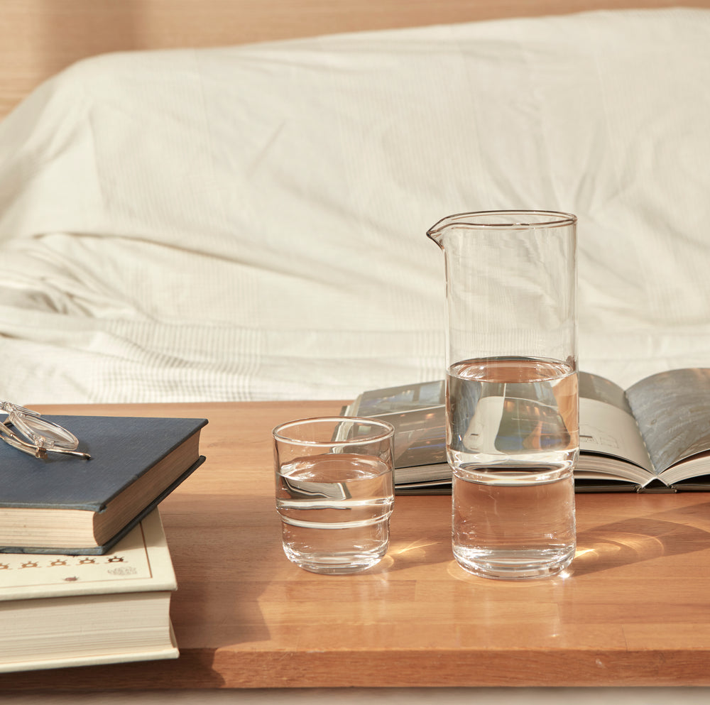 A set of 1 litre cylindrical minimalistic and stylish clear handmade glass carafe and matching drinking glasses on a couch table