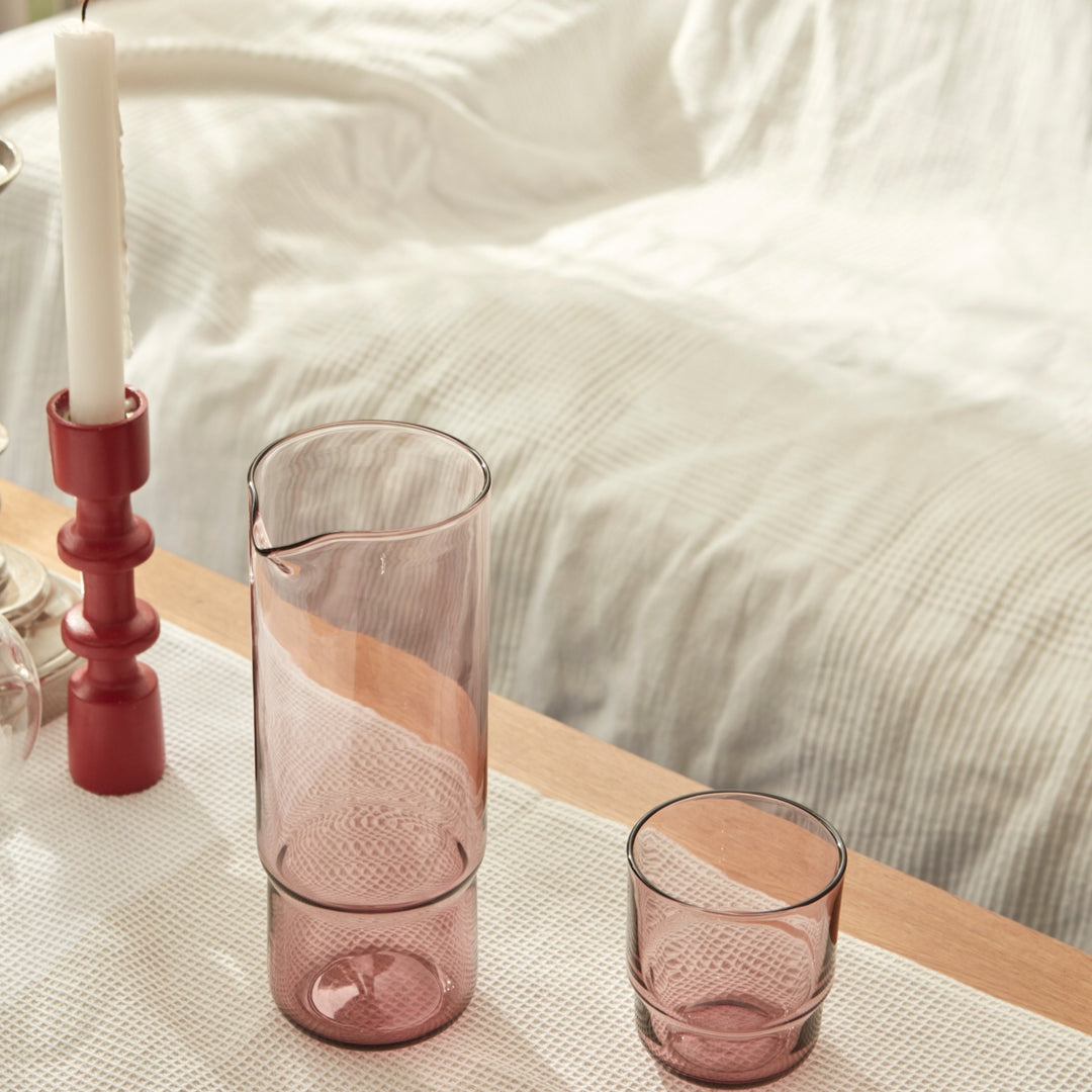 A set of minimalistic pastel pink handmade glass carafe and matching drinking glass on a couch table