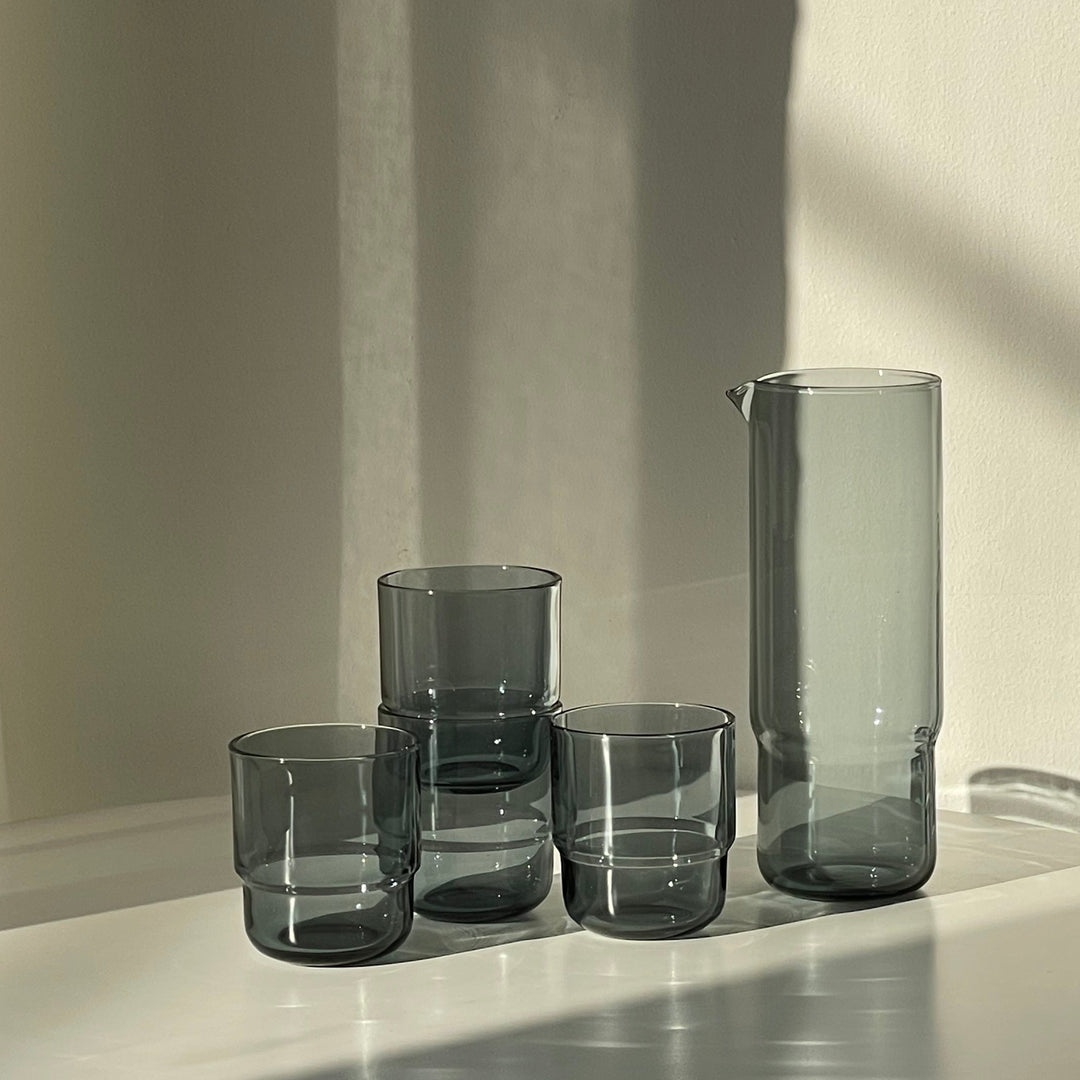 A set of minimalistic handmade glass carafe and matching stackable drinking glasses in blue-grey