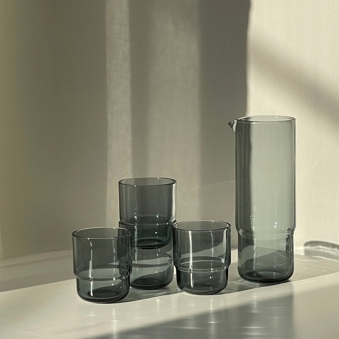 Minimalistic glass carafe and matching stackable drinking glasses in blue-grey