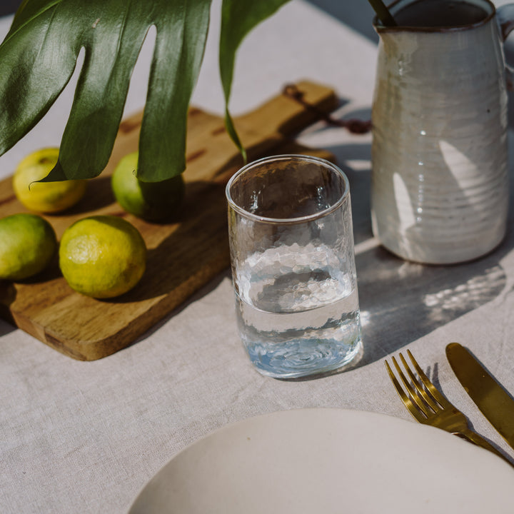 A big and tall 400ml clear drinking glasses with a unique shape and hammered texture on an outdoor summer table