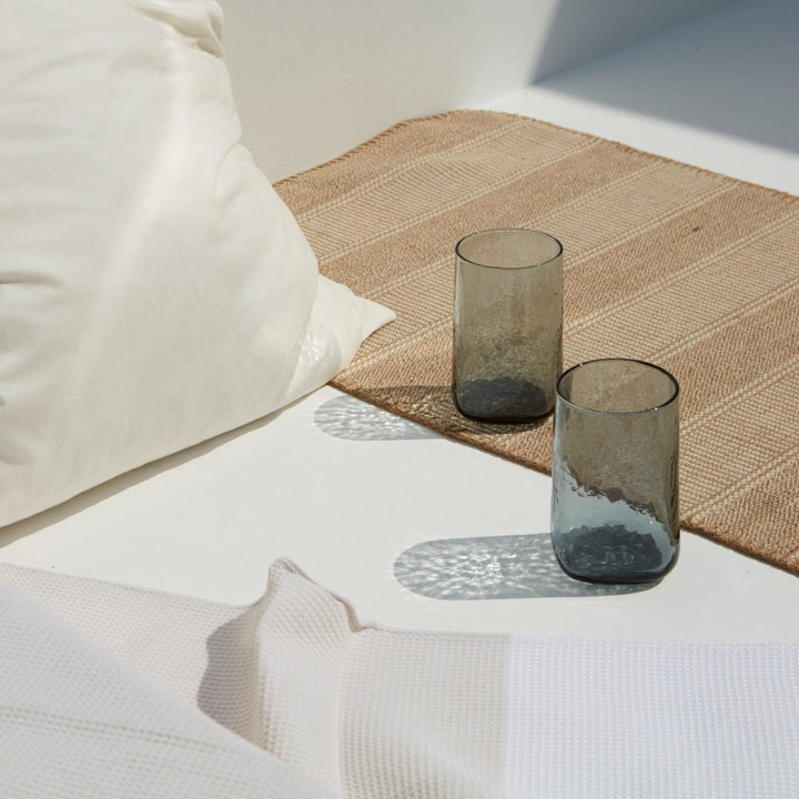 Big smoke grey drinking glass with a unique shape and hammered texture in a summery setting